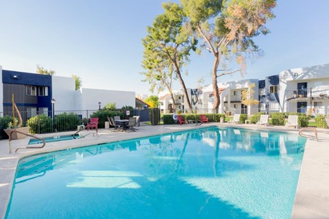 A swimming pool in front of a building with trees and chairs around it.