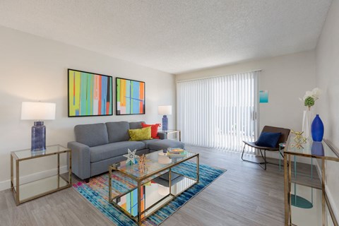 A living room with a grey couch, a glass coffee table, and a painting on the wall.