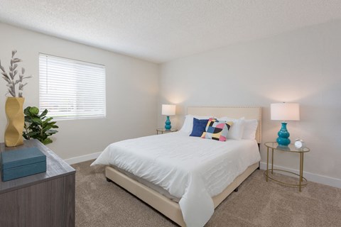 A bedroom with a white bed and a blue lamp on a side table.