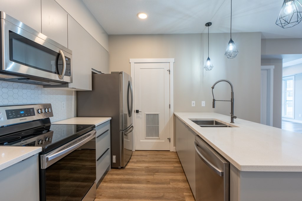 A modern kitchen with stainless steel appliances and wooden flooring.