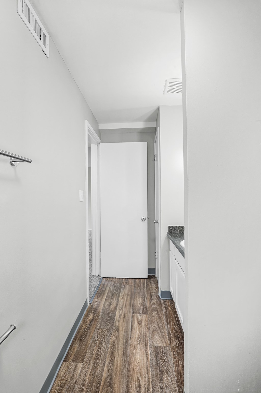 A white hallway with a wooden floor and a white door.