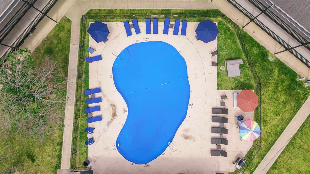 An aerial view of a blue swimming pool surrounded by a grassy area and a concrete walkway.