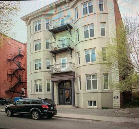A black SUV is parked on the sidewalk in front of a two-story building with a balcony.