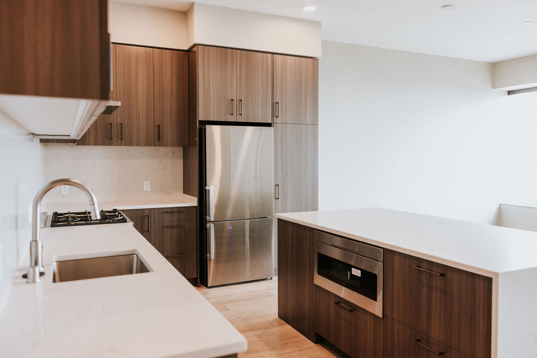 Kitchen in dark color scheme features quartz countertops, upgraded appliances and waterfall edge island.