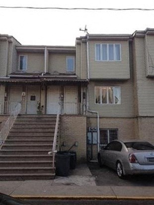 A silver car is parked in front of a two-story house.