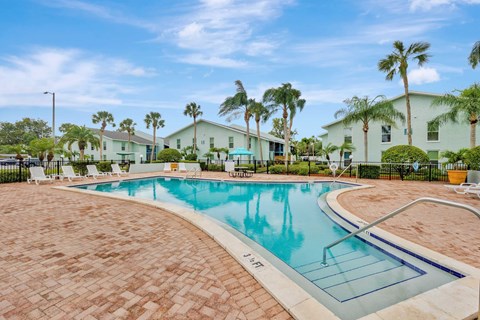 A swimming pool surrounded by palm trees and a white building.