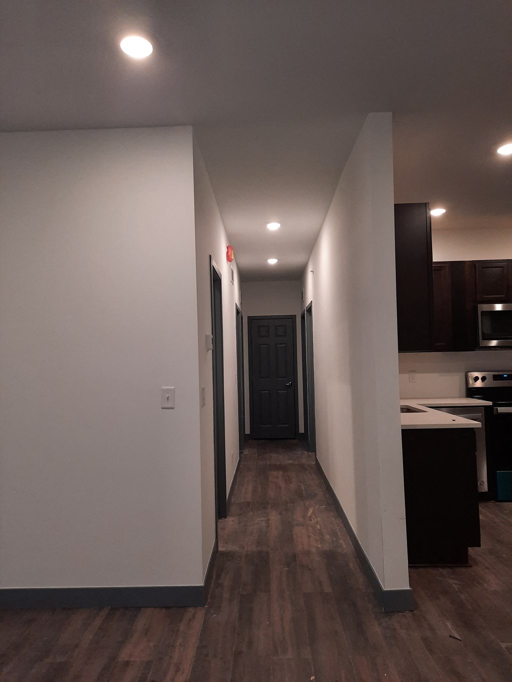 a long hallway with white walls and a door to a kitchen