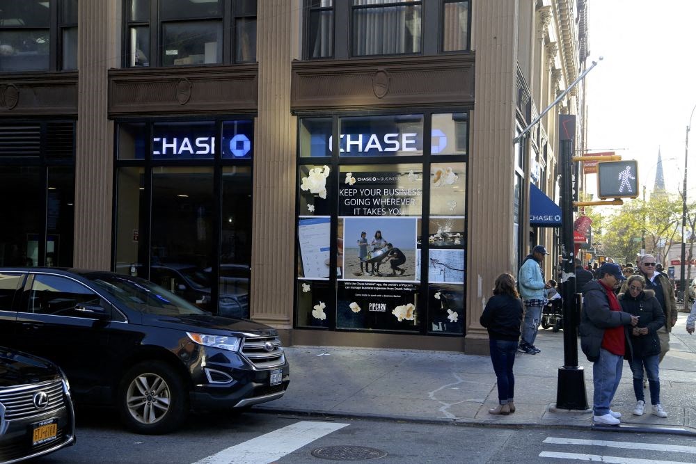 people waiting to cross a street in front of a chase building