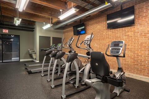 A gym with treadmills and a brick wall.