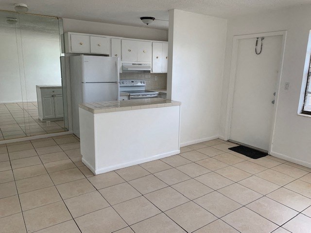 an empty kitchen with white cabinets and a refrigerator