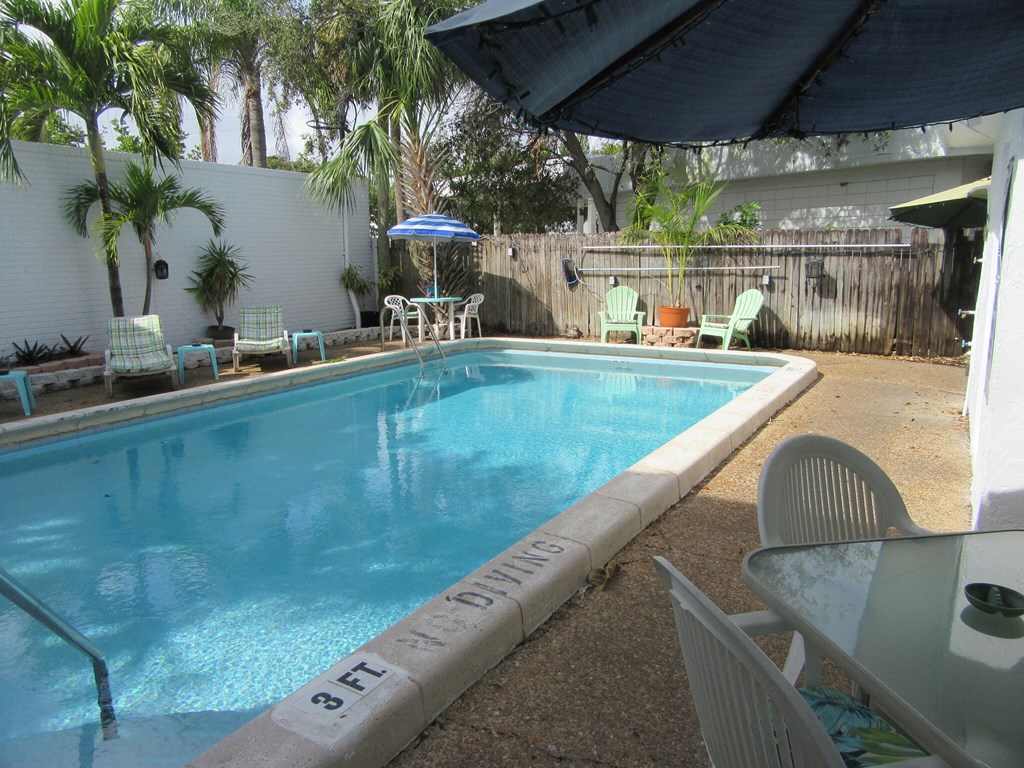 the pool is next to a patio with chairs and an umbrella