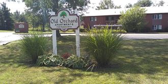 a sign for old orchard apartments in front of some plants