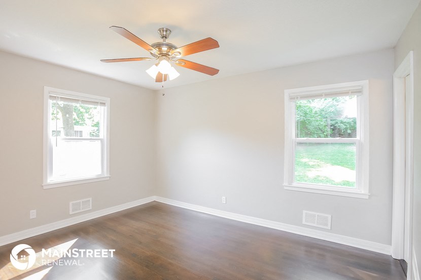 an empty room with a ceiling fan and two windows