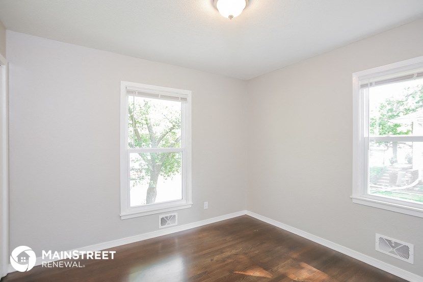 a bedroom with a hardwood floor and two windows