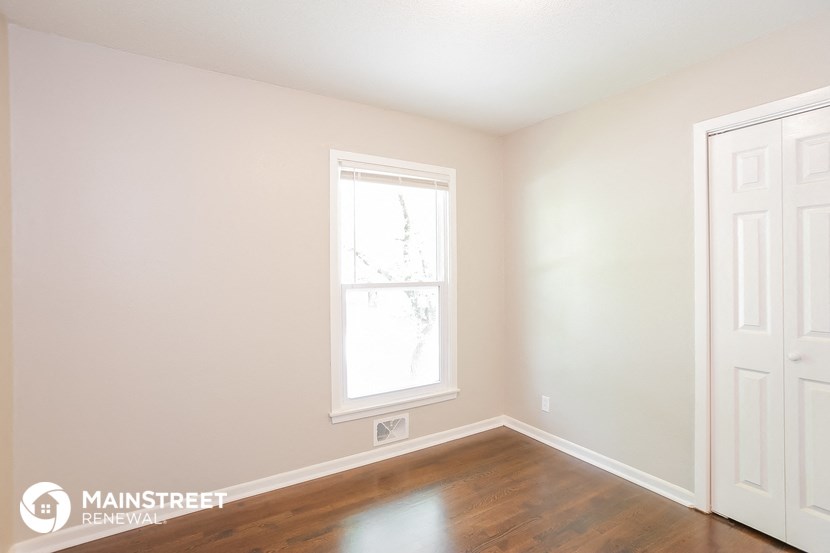 a bedroom with white walls and wood floors and a window