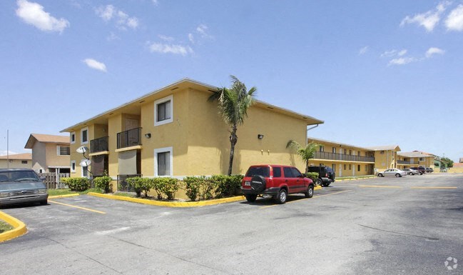 a yellow apartment building with cars parked in a parking lot
