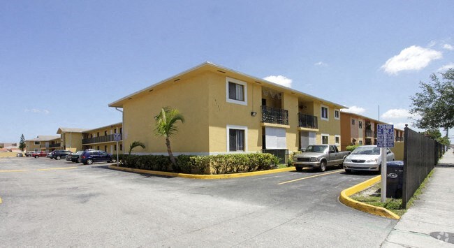 a yellow apartment building with cars parked in a parking lot
