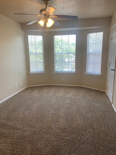 an empty living room with a ceiling fan and three windows