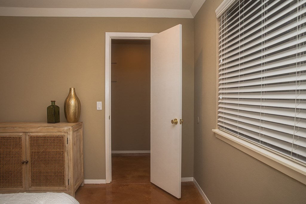 a bedroom with white blinds on the window and a door to a hallway