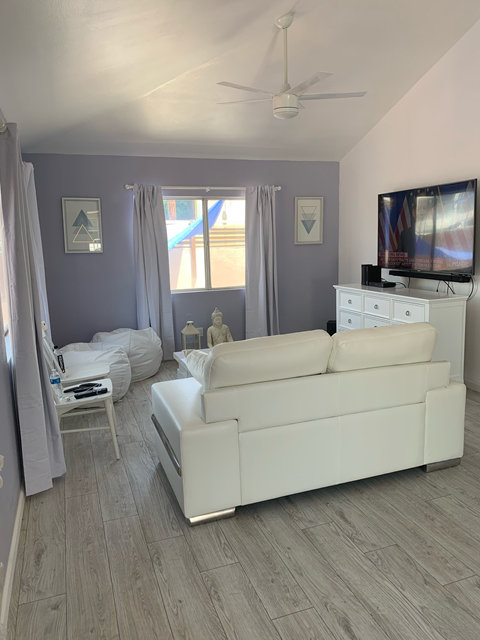 A living room with a white couch and a television on top of a white cabinet.