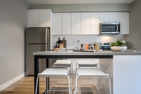 a kitchen with white cabinets and a counter with three white stools