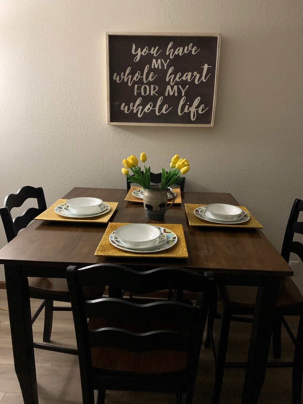 the dining table is set with plates and a vase with yellow flowers on it