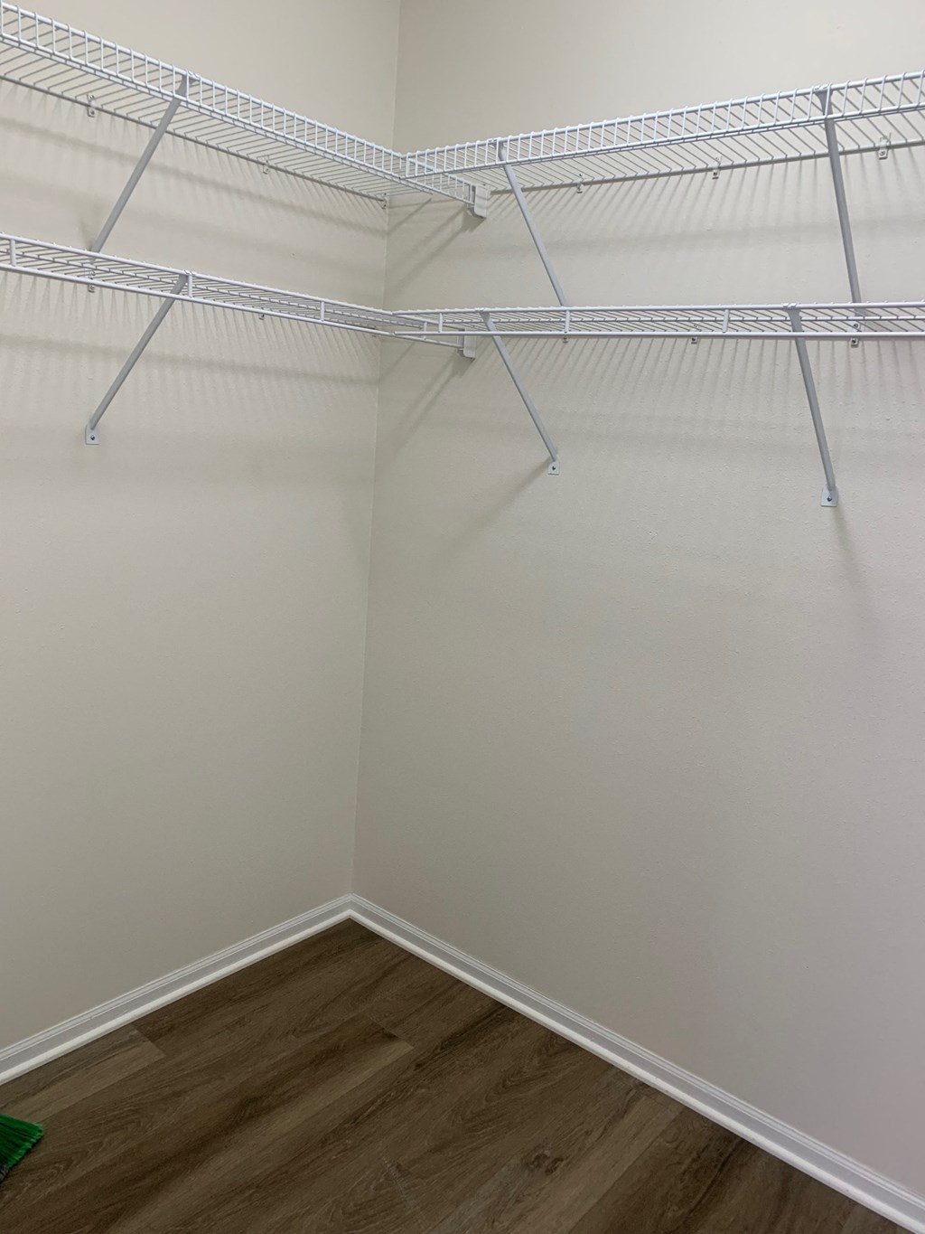 a walk in closet with white walls and shelves and a wooden floor