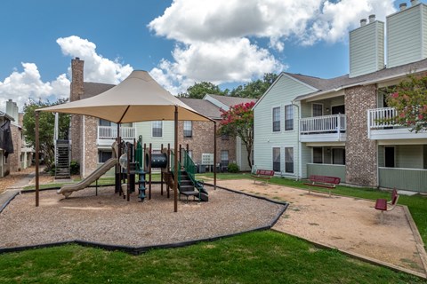 A playground with a slide and a swing set in the middle of a grassy area.