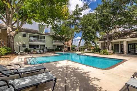 A swimming pool surrounded by trees and benches in a sunny day.