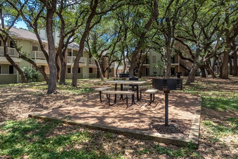 A picnic table is set up in a courtyard with a grill and apartment buildings in the background.