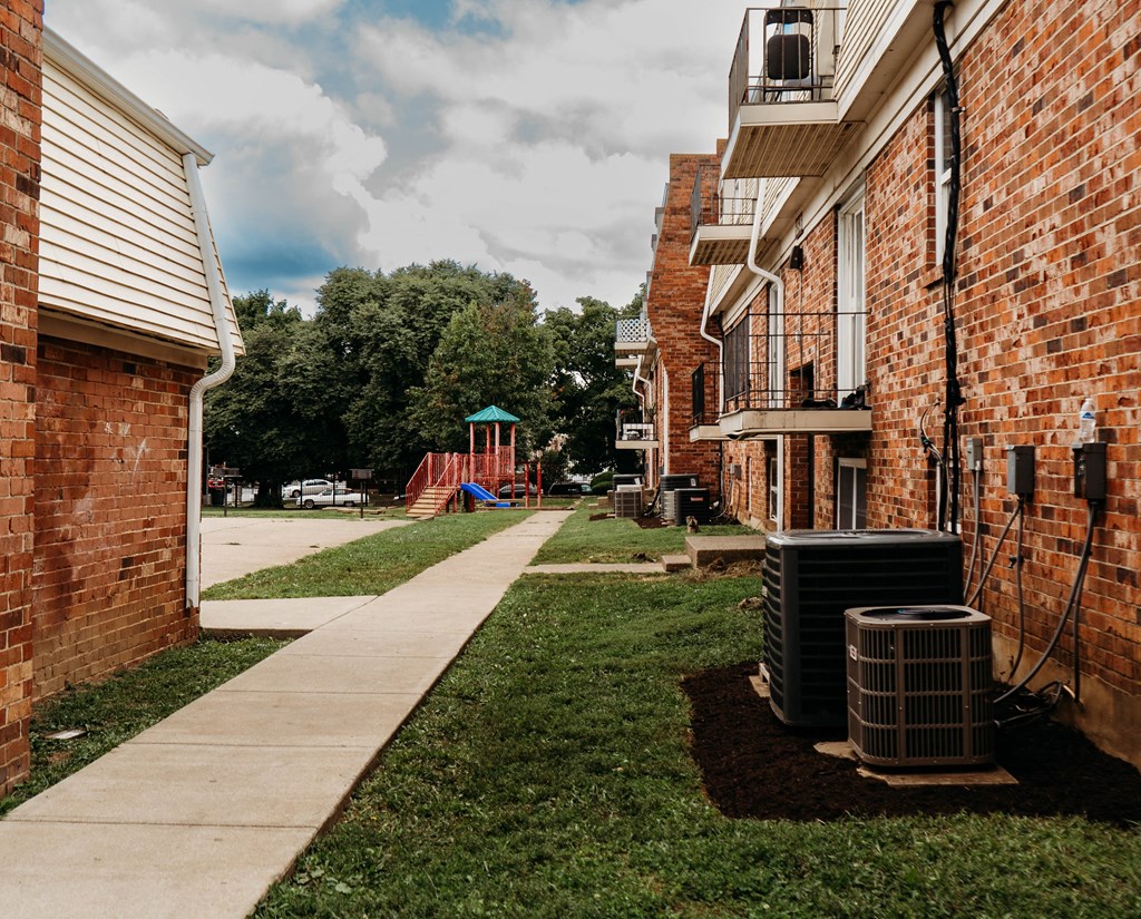a sidewalk between two brick buildings with a playground in the background