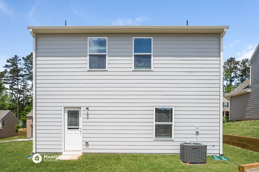 the side of a white house with two windows and a trash can