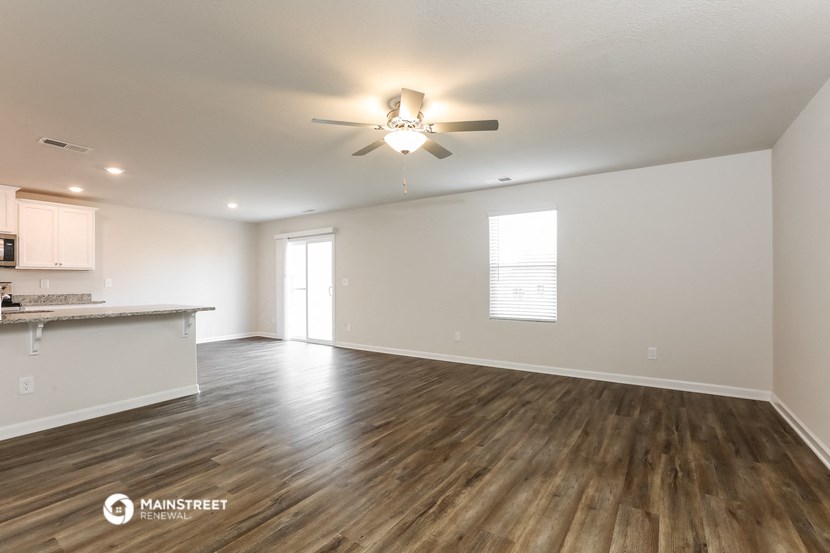 the living room and kitchen of an apartment with wood flooring and a ceiling fan