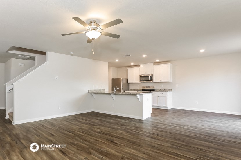 the living room and kitchen of an apartment with a ceiling fan