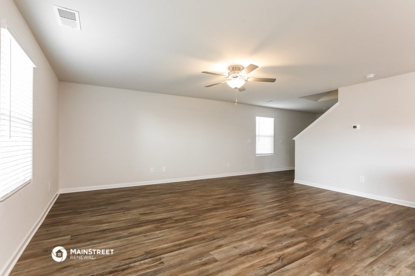 the spacious living room with hardwood flooring and a ceiling fan