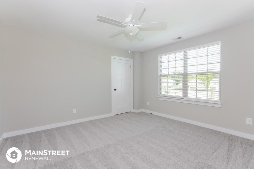 the spacious living room with white carpet and a ceiling fan