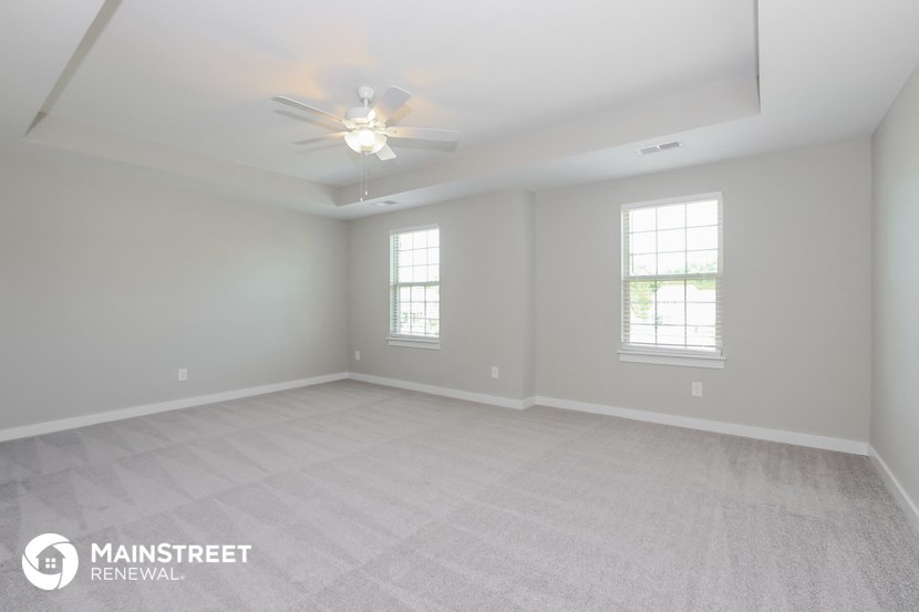 the spacious living room with ceiling fan and two windows