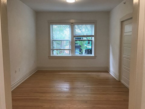 A room with wooden floors and a window with blinds.