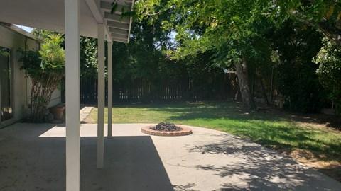 A patio with a fire pit and trees in the background.