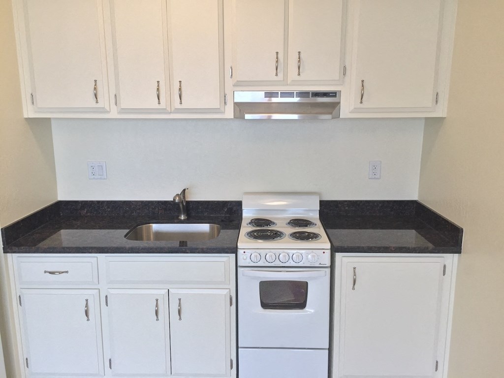 an empty kitchen with white cabinets and a stove and sink
