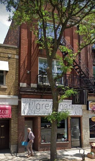 A man is walking on the sidewalk in front of a building with a tree.