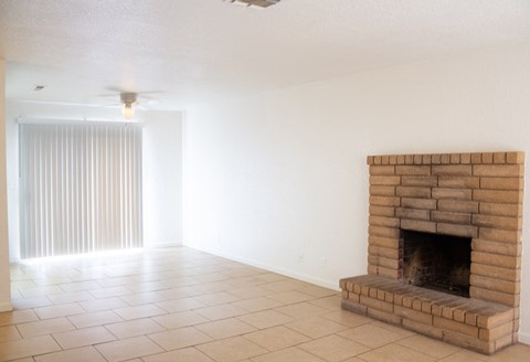 an empty living room with a brick fireplace and a ceiling fan
