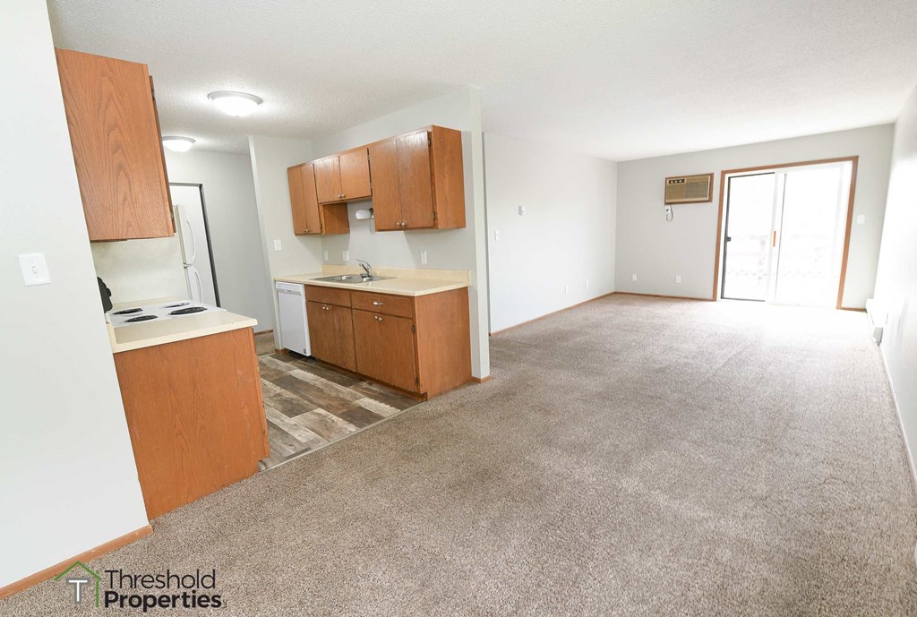a kitchen and living room with a carpeted floor and wooden cabinets