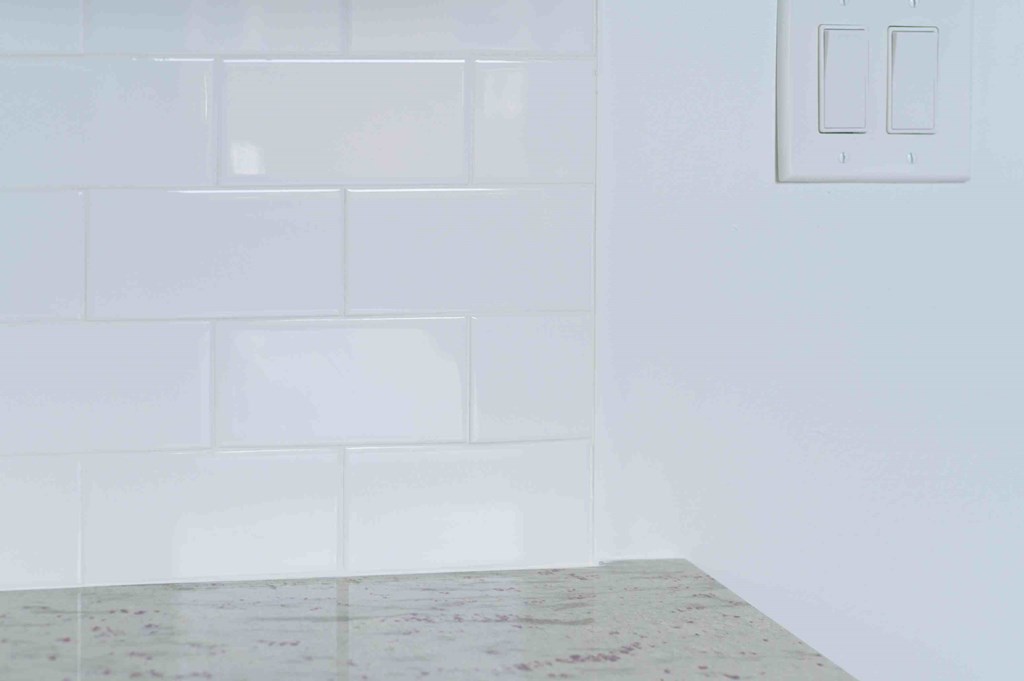 a white tiled bathroom with a light switch on the wall