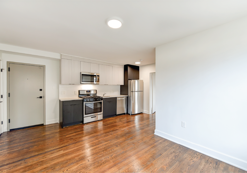 an empty living room and kitchen with wood floors and white walls