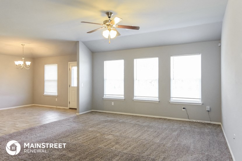 an empty living room with a ceiling fan and windows