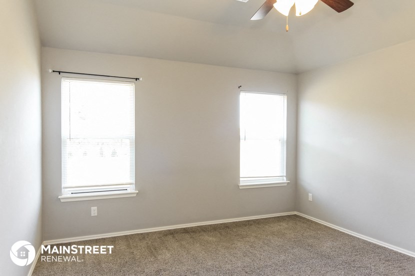 an empty room with two windows and a ceiling fan
