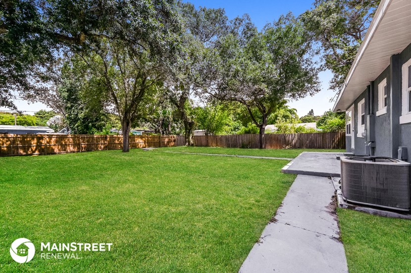 a backyard with a sidewalk and trees and a house