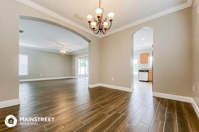 an empty living room with hardwood flooring and a chandelier
