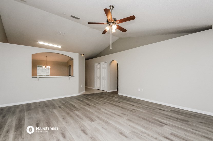 the spacious living room with ceiling fan and white walls
